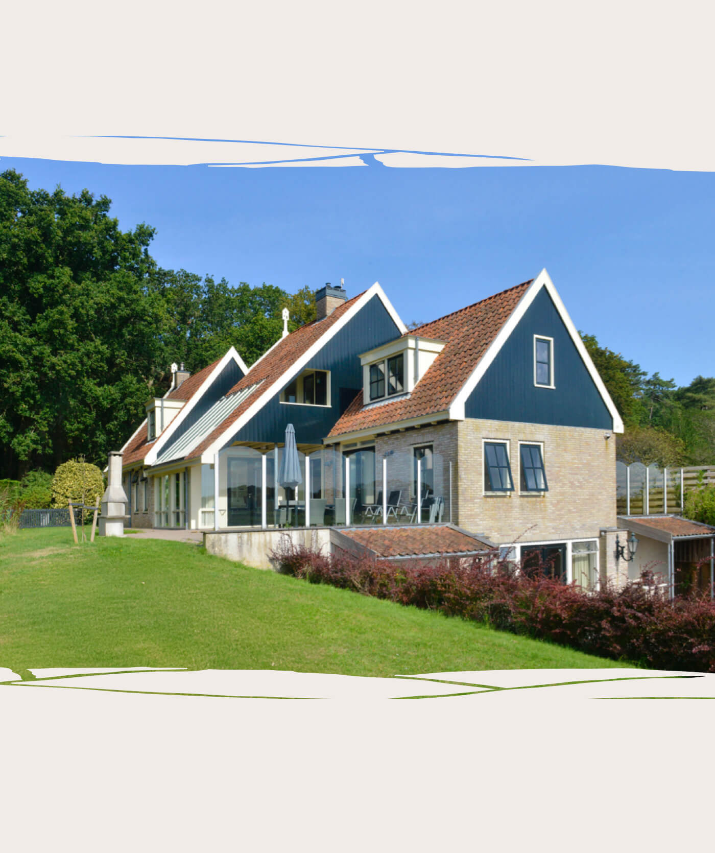 Een modern huis met grote ramen, een rood pannendak en een zwart-witte buitenkant staat op een met gras begroeide helling, omringd door groen. De perfecte inspiratie voor webshops of websites die stijlvol wonen onder een helderblauwe hemel willen laten zien.