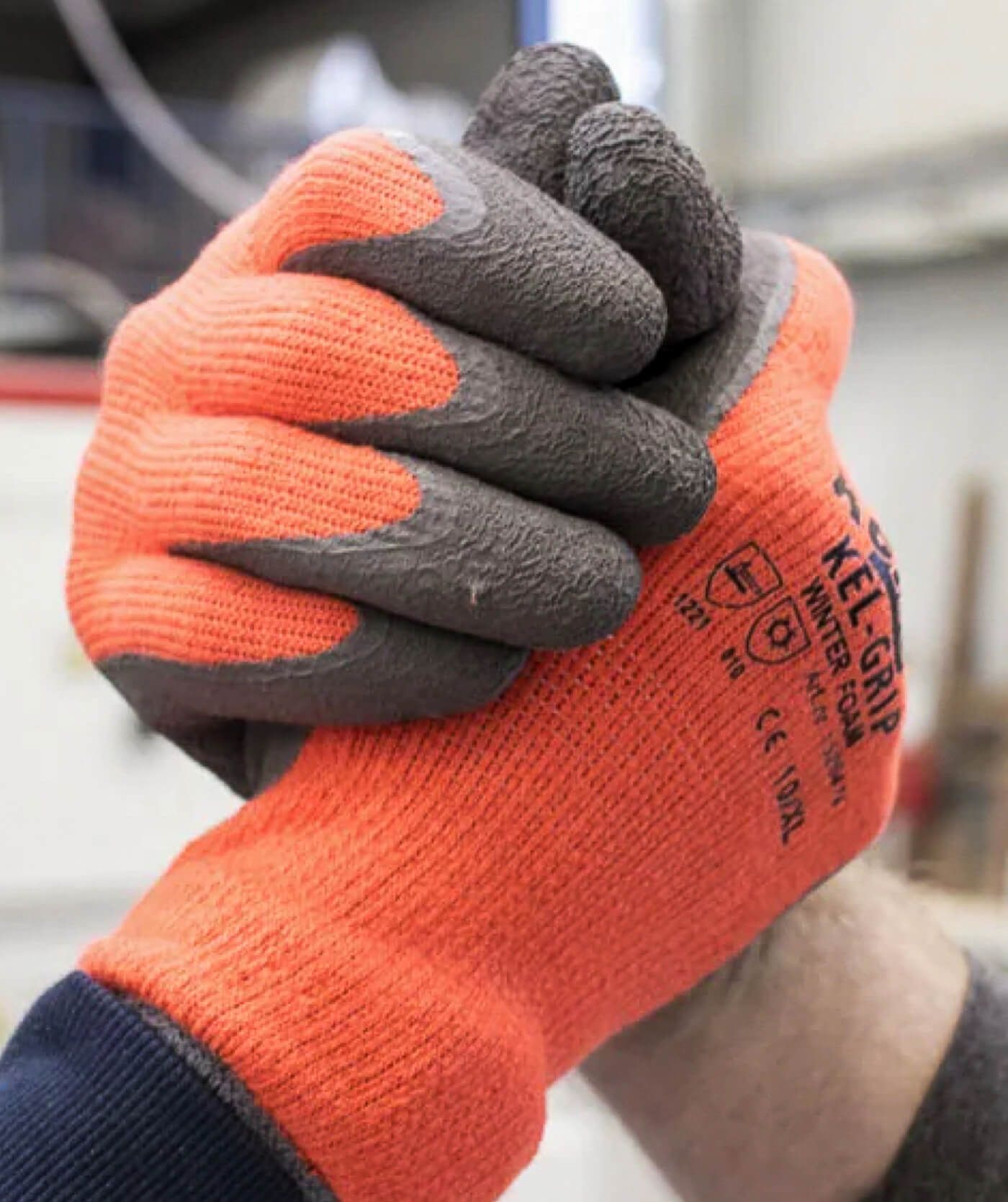Twee mensen met oranje en grijze werkhandschoenen schudden elkaar de hand, wat symbool staat voor teamwork of partnerschap in een industriële omgeving. Perfect voor webshops of online diensten die gericht zijn op samenwerking en vertrouwen.