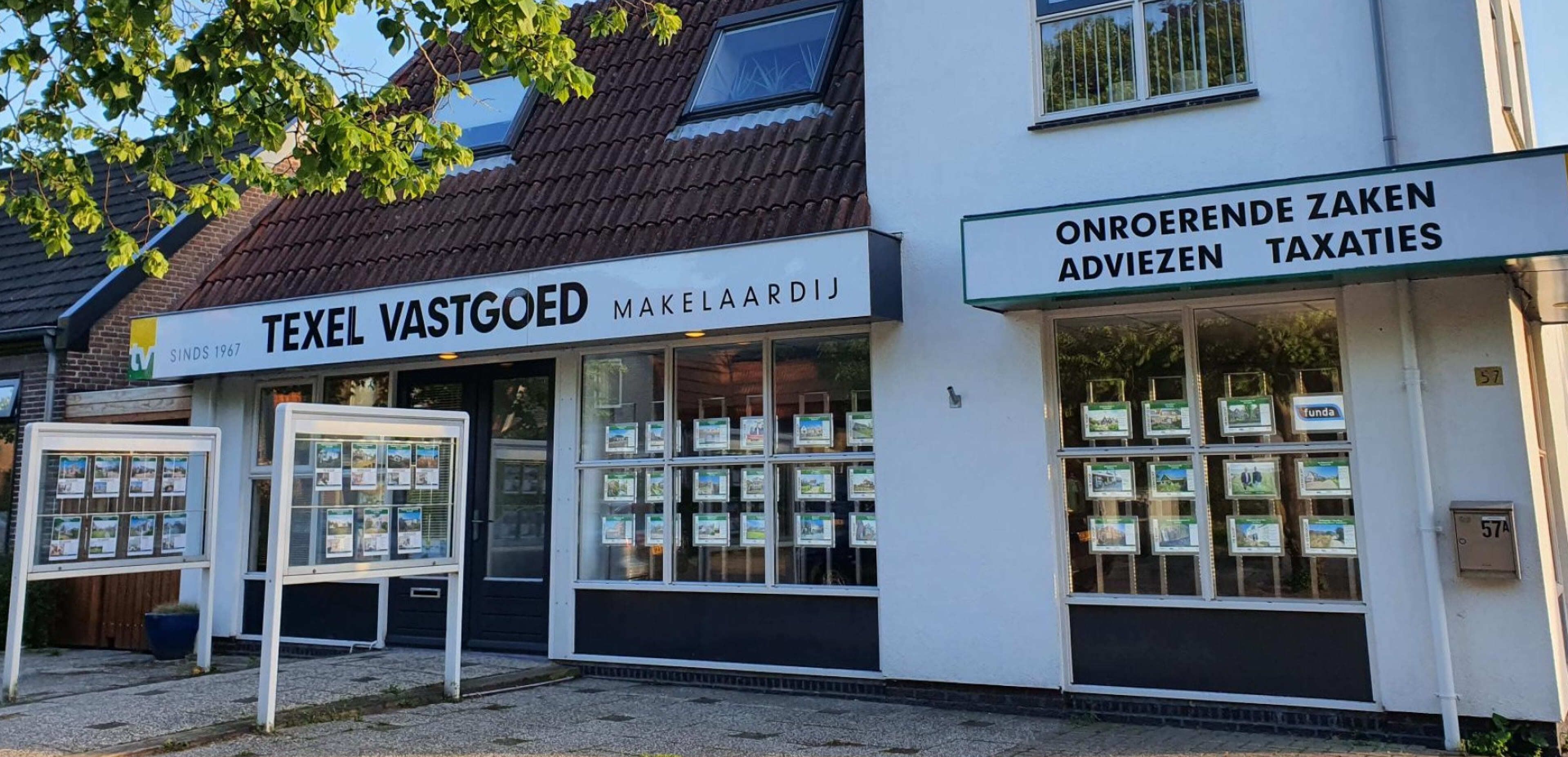 Een makelaarskantoor met grote ramen toont tal van vastgoedadvertenties en promoot onlinediensten; op de borden staat “Texel Vastgoed Makelaardij” en “Onroerende Zaken Adviezen Taxaties.”.