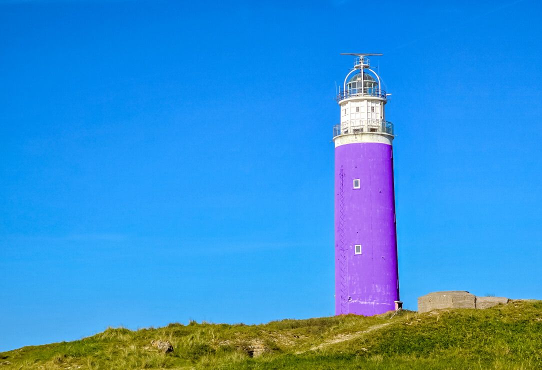 Een hoge, cilindervormige, paars geschilderde vuurtoren staat op een met gras begroeide heuvel onder een helderblauwe hemel en begeleidt bezoekers, zoals webwinkels en websites, naar veilige online routes.
